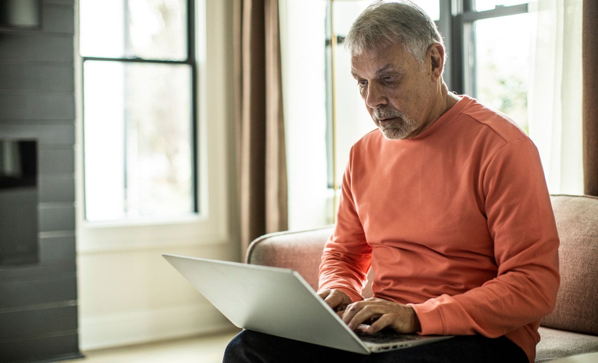 A senior man views advertisements on his laptop while he sits on a sofa.